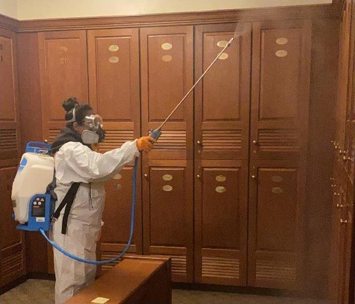 SERVPRO team member, donned in PPE, applying disinfecting spray in locker room